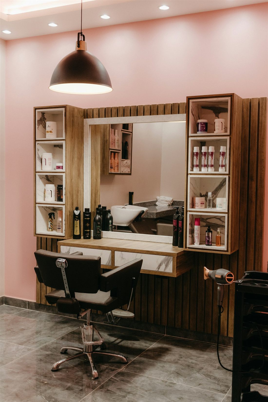Rincón de peluquería con pared rosada, tocador de madera, espejo y sillón