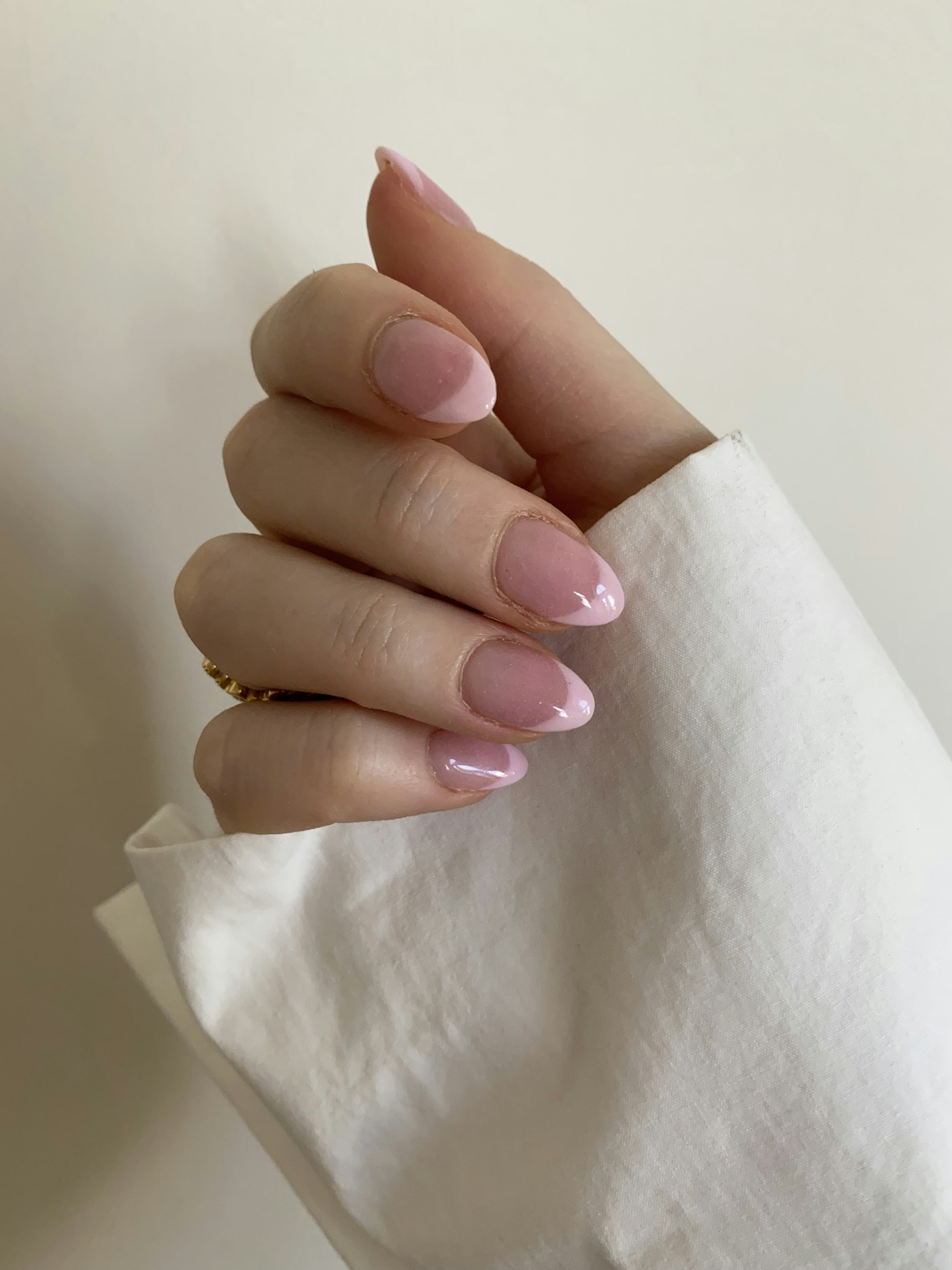 Mano con manicura francesa rosa suave sobre una tela blanca